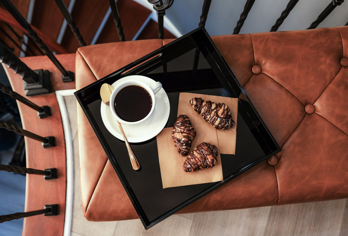 Coffee and pastries on a black tray atop a leather bench at Gaspar’s Luxury Estate in South Tampa