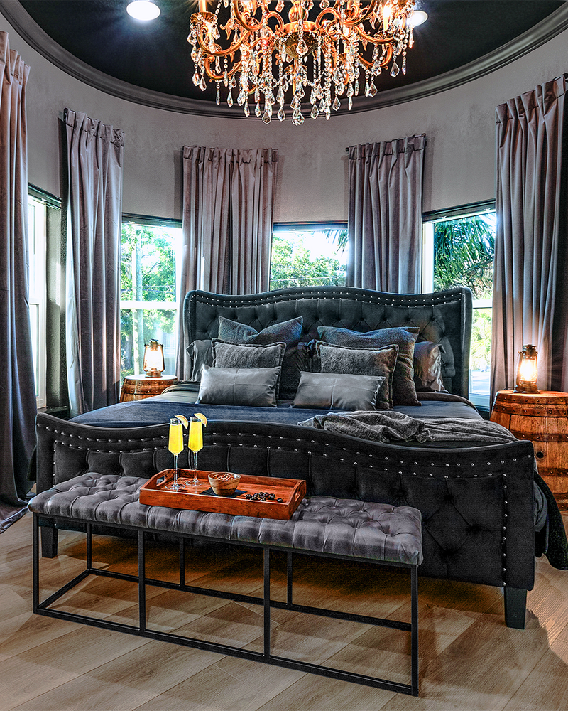 Gaspar’s Quarters king suite in Tampa featuring a gold crystal chandelier, storm-sky mural, and rustic barrel nightstands.