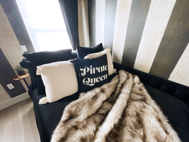Pirate Queen bed staging in the Calypso Suite at Gaspar's Estate Tampa with striped walls and a faux fur throw.